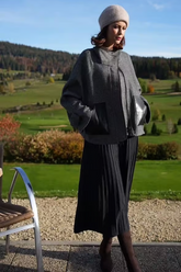 a lady in a grey wool coat and a black pleated skirt